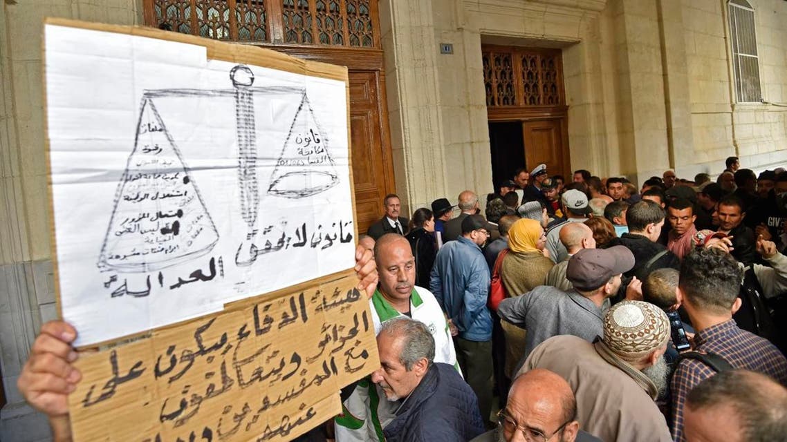 Algerians lift a placard demanding justice as they wait at the main public entrance of Sidi M’hamed court in the capital Algiers on December 2, 2019, ahead of the opening of a corruption trial of former political and business figures. (AFP)