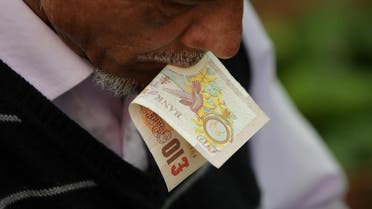 A trader holds a ten pound sterling note in his mouth as he prepares a customer's order at Whitechapel Market in east London. (File photo: AFP)