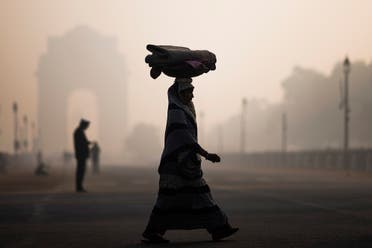 A woman balances a load on her head as she crosses a street near India Gate in heavy smoggy conditions in New Delhi. (File photo: AFP)