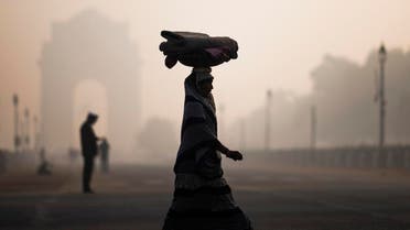 A woman balances a load on her head as she crosses a street near India Gate in heavy smoggy conditions in New Delhi. afp