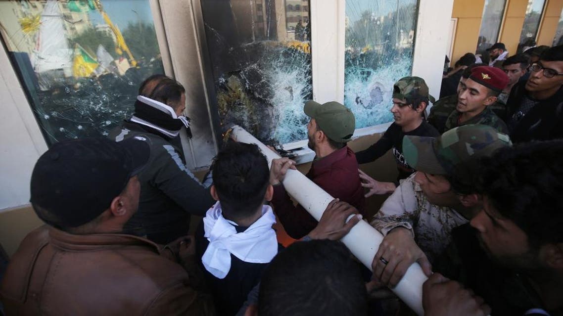 Iraqi protesters use a plumbing pipe to break the bullet-proof glass of the US embassy's windows in Baghdad. (AFP)