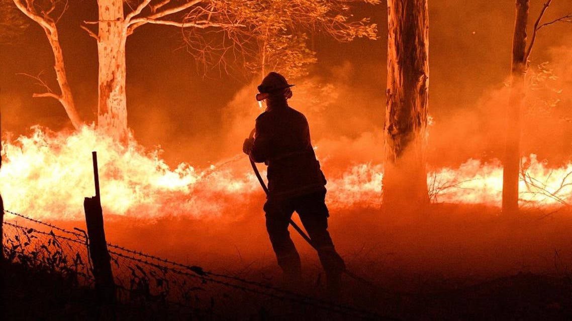 A firefighter hosing down trees and flying embers in an effort to secure nearby houses from bushfires in Australia. (AFP)