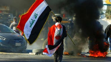 A demonstrator carries an Iraqi flag as he walks near burning tires, during ongoing anti-government protests in Najaf, Iraq January 12, 2020. (Reuters)