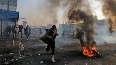 An anti-government protester wearing a gas mask runs hold his mask past flaming tires and through tear gas fumes at the scene of clashes with security forces in Tayaran Square. (AFP)