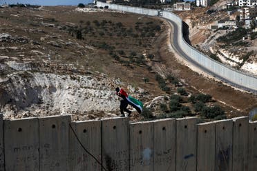 A Palestinian covered with national flag walks on top of the Israeli wall separating the West Bank city of Abu Dis from east Jerusalem. (File photo: AFP)
