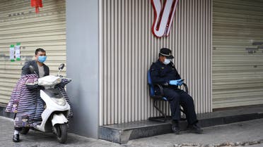 A security officer wearing a face mask checks his phone while sitting outside a closed shop in China. (Reuters)