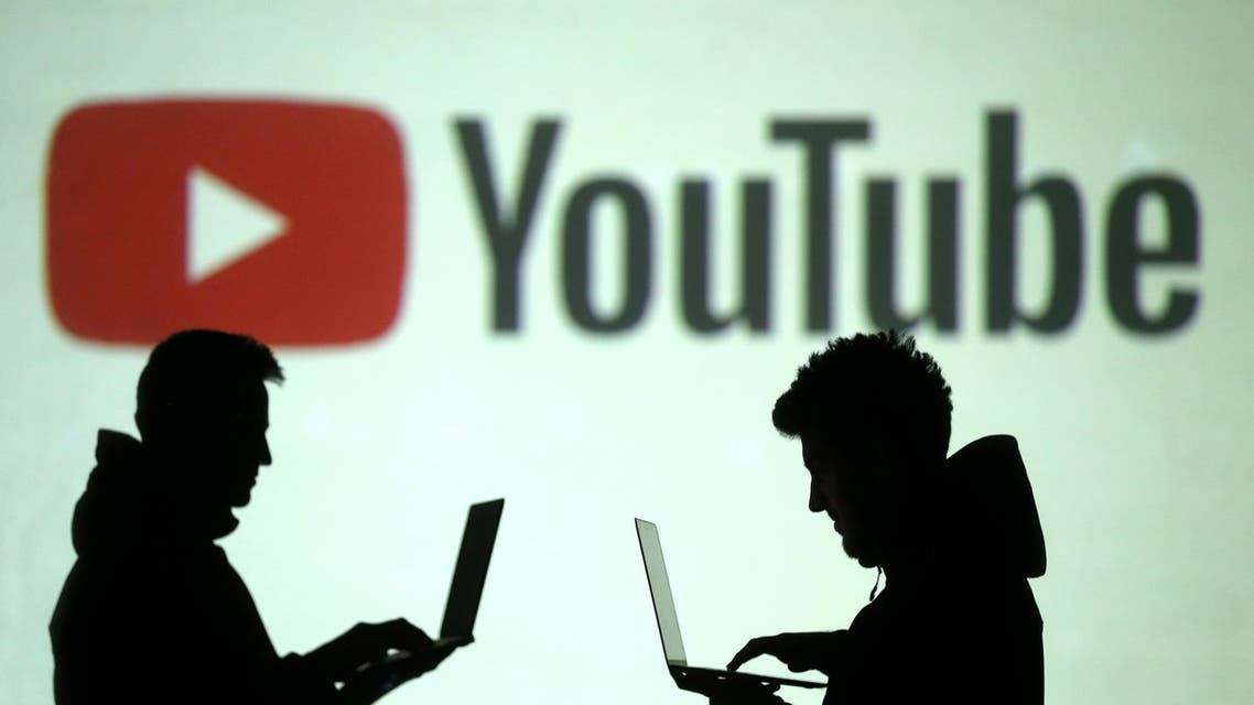 Silhouettes of mobile device users are seen next to a screen projection of Youtube logo, March 28, 2018. (Reuters)