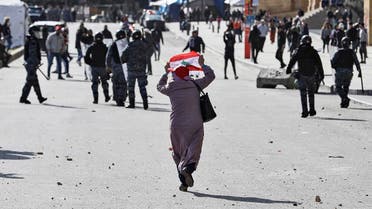 An elderly woman raises a Lebanese national flag behind riot police during clashes with anti-government protesters. (AFP)