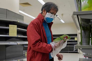 رجل يرتدي قناع طبي وكيس من البلاستيك وهو يعاين أحد المنتجات في سوبر ماركت بهونغ كونغ