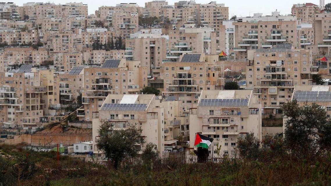 A demonstrator holds a Palestinian flag as the Jewish settlement of Modiin is seen in the background, during a protest against Trump's Middle East peace plan. (Reuters)