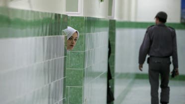 An Iranian inmate peers from behind a wall as a guard walks by at the female section of the infamous Evin jail, north of Tehran, 13 June 2006. AFP PHOTO/ATTA KENARE