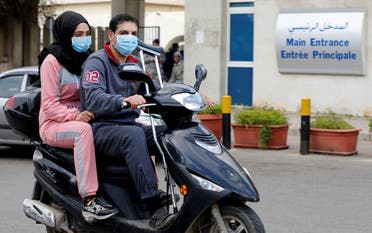 People wearing face masks ride on a motorbike outside Rafik Hariri hospital, where Lebanon's first coronavirus case is being quarantined, in Beirut. (Reuters)