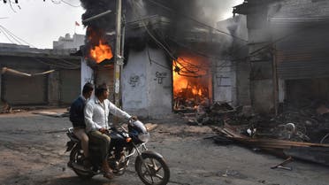A motorcyclist drives past shops that were set on fire by mobs in New Delhi on Feb. 26, 2020. (Photo: AP)