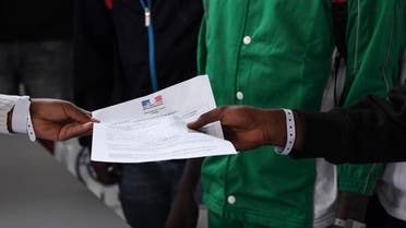 Asylum seekers who have been rescued by the Aquarius rescue ship and another ship in the Mediterranean sea, hold an official document delivered by the French embassy in Malta, as they queue upon their arrival at Roissy-Charles de Gaulle airport, in Roissy-en-France, north of Paris, on August 30, 2018. (AFP)