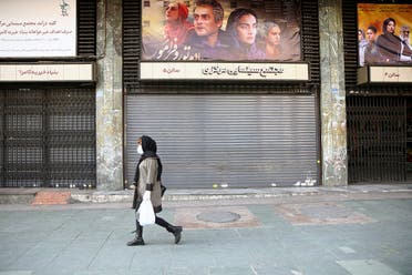 An Iranian woman wears a protective mask to prevent contracting coronavirus, as she walks on a street in front of a closed cinema in Tehran. (Reuters)