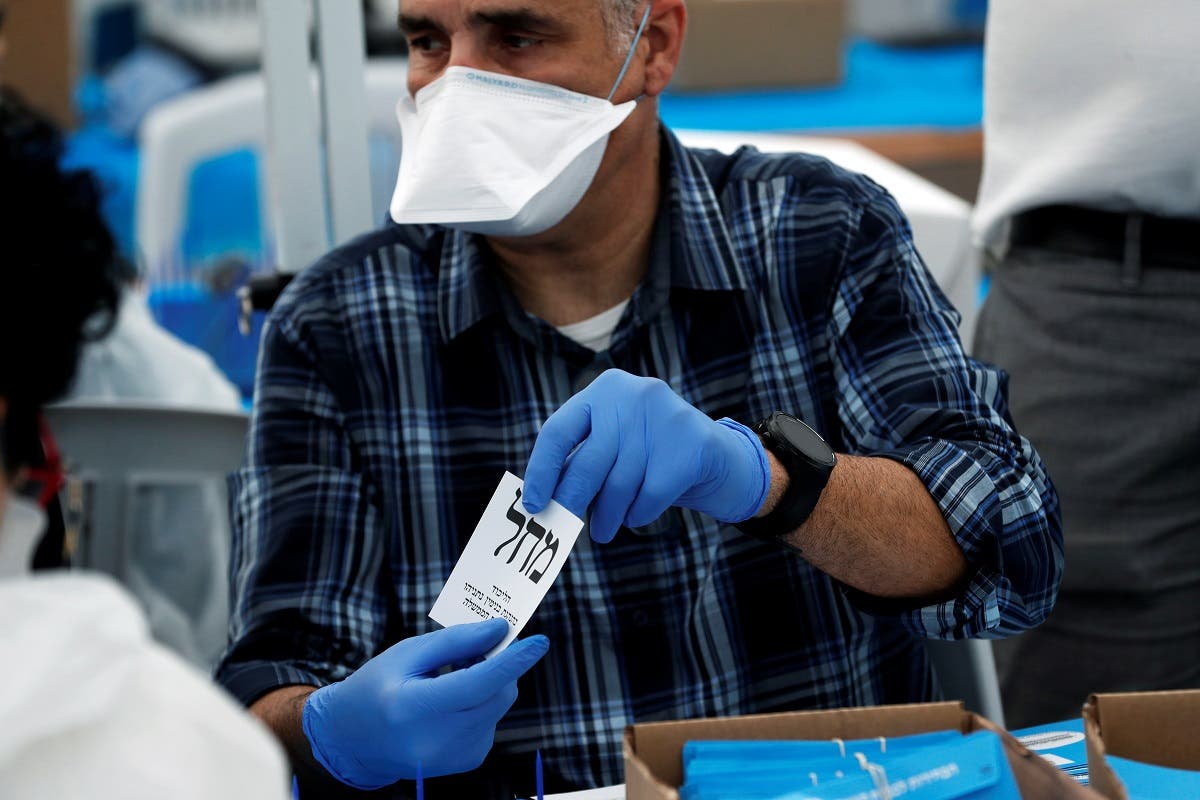 An Israeli election monitor wearing a mask and gloves holds a ballot for the Likud party as votes cast by Israelis in home-quarantine over coronavirus concerns following Israel's national election are tallied, in Shoham. (Reuters)