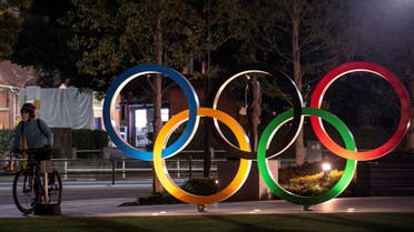 A woman wearing a protective face mask, following the outbreak of the coronavirus, rides her bicycle past The Olympic rings in front of the Japan Olympics Museum in Tokyo, Japan, March 3, 2020. (Reuters)