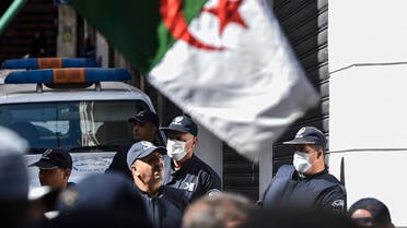 Algerian anti-riot police members wearing protective health masks stand as protesters march past them during a weekly anti-government demonstration in the capital Algiers on March 6, 2020. (AFP)