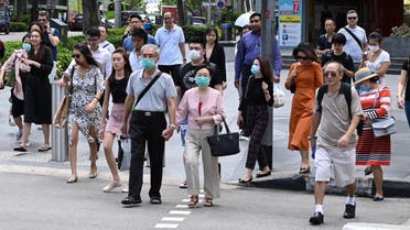 People, some wearing a protective facemask amid fears about the spread of the COVID-19 novel coronavirus, crosses the road in Singapore on February 26, 2020. (Photo by Roslan RAHMAN / AFP)