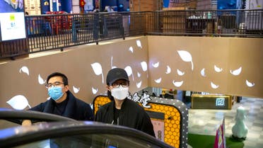A couple wear face masks as they ride an escalator at a shopping mall in Beijing, Saturday, March 7, 2020.