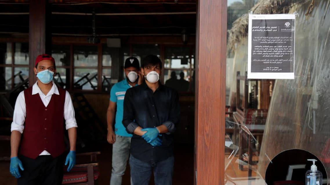 Mask-clad workers stand inside a closed-down cafe in Qatar's capital Doha on March 16, 2020. (AFP)