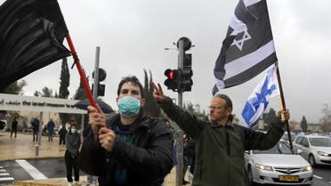 A man waves an Israeli flag and another Israeli flag with the colors inverted standing next to another mask-clad man waving a plain black banner, during a protest outside the Knesset (parliament) in Jerusalem on March 19, 2020. (AFP)