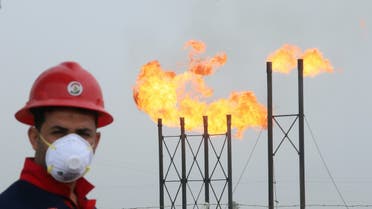 Flames emerge from flare stacks at Nahr Bin Umar oil field, as a worker wears a protective mask, following an outbreak of coronavirus, north of Basra, Iraq, March 15, 2020. (Reuters)