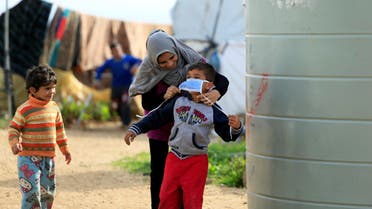 A Syrian refugee woman puts a face mask on a boy as a precaution against the spread of coronavirus, in al-Wazzani area, in southern Lebanon, March 14, 2020. (Reuters)