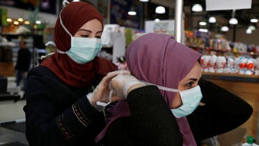 A Palestinian cashier is helped by her colleague to wear a mask amid coronavirus precautions, in a supermarket in Gaza City March 8, 2020. Picture taken March 8, 2020. REUTERS/Mohammed Salem