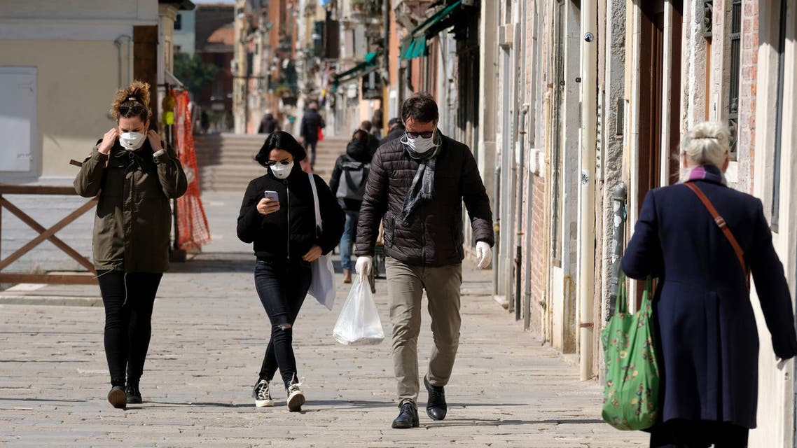 مواطنون يضعون قناعات واقية يسيرون في شارع بالبندقية يوم 25 مارس