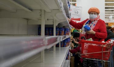 A woman, wearing a protective mask, holds a pack of buckwheat from a new delivery, next to empty shelves in a section for cereals and groats, in a supermarket in Moscow, Russia on March 19, 2020. (Reuters)