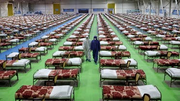 People in protective clothing walk past rows of beds at a temporary 2,000-bed hospital for COVID-19 coronavirus patients set up by the Iranian army at the international exhibition center in northern Tehran, Iran, on Thursday, March 26, 2020. (AP Photo/Ebrahim Noroozi)