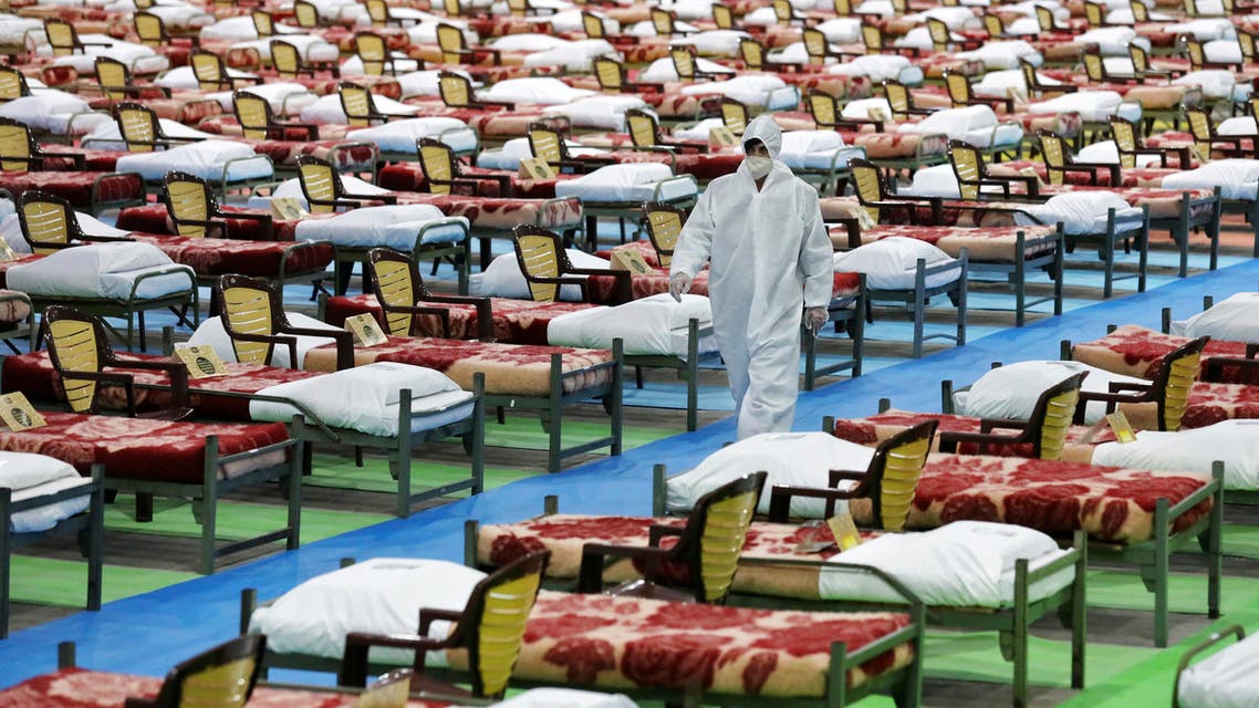 People in protective clothing walk past rows of beds at a temporary 2,000-bed hospital for COVID-19 coronavirus patients set up by the Iranian army at the international exhibition center in northern Tehran, Iran, on Thursday, March 26, 2020. (AP Photo/Ebrahim Noroozi)