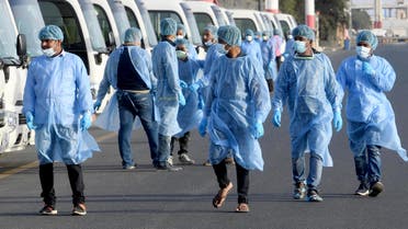 Health ministry workers, wearing protective outfits, wait on the tarmac of the Kuwait international Airport to receive Kuwaitis returning from Frankfurt on March 26, 2020, to be taken to a hospital for novel coronavirus checkups, in the capital Kuwait City.