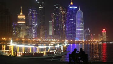 In this Tuesday, May 14, 2019 photo, two people take in the sea breeze at the Corniche waterfront promenade in Doha, Qatar, with a night view of skyline. (AP Photo/Kamran Jebreili)