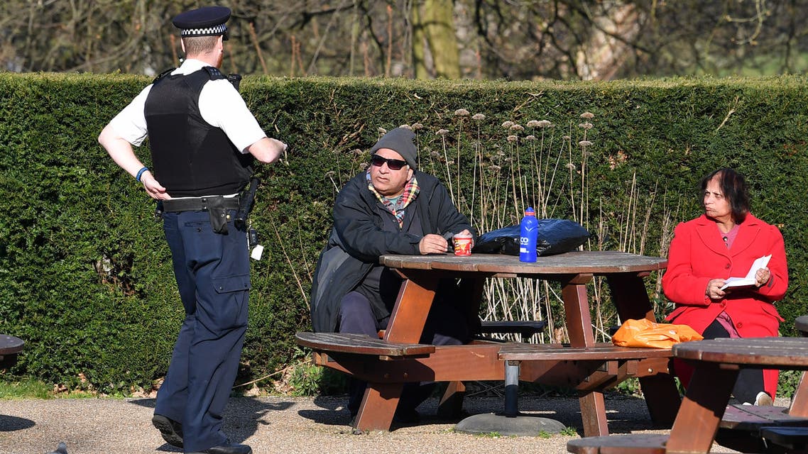 A police officer speaks to a couple sat at a bench in the sunshine in Greenwich Park in London on March 26, 2020 after the government ordered a lockdown to help stop the spread of the new coronavirus. Britain's leaders have urged people to respect an unprecedented countrywide lockdown, saying that following advice to stay at home would stop people dying of coronavirus.