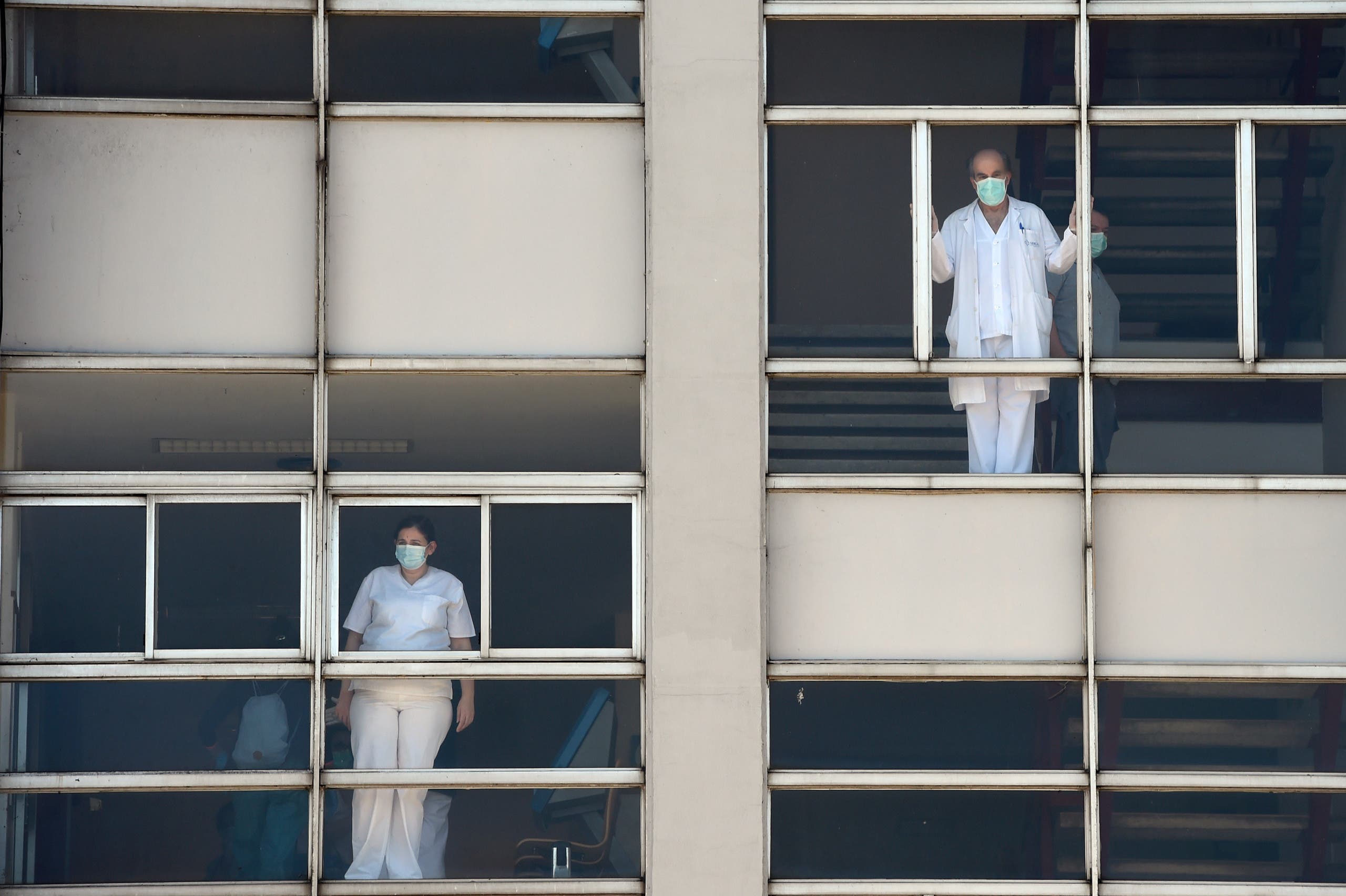 Healthcare workers dealing with the new coronavirus crisis look through the windows of the University Hospital in Coruna, northwestern Spain, on March 26, 2020. (AFP)