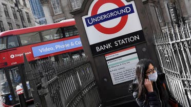 FILE PHOTO: A woman wearing a protective face mask walks out of an underground tube station in the City of London financial district, whilst British stocks tumble as investors fear that the coronavirus outbreak could stall the global economy, London, Britain, March 9, 2020. REUTERS/Toby Melville/File Photo