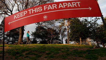 A woman jogs in Brooklyn's Fort Greeene park, Sunday, April 5, 2020, beneath a sign demonstrating the distance people should keep from each other during the coronavirus outbreak in New York. People have been urged to cover their faces and stay at least six feet apart during to avoid contracting COVID-19. (AP 