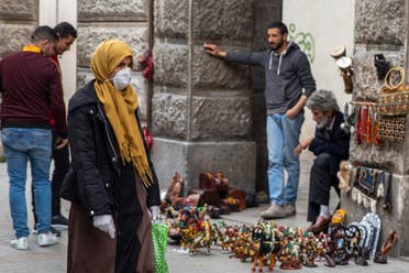 A woman wearing a mask walks past street vendors Tuesday, March 17, 2020 in Tunis. (AP)