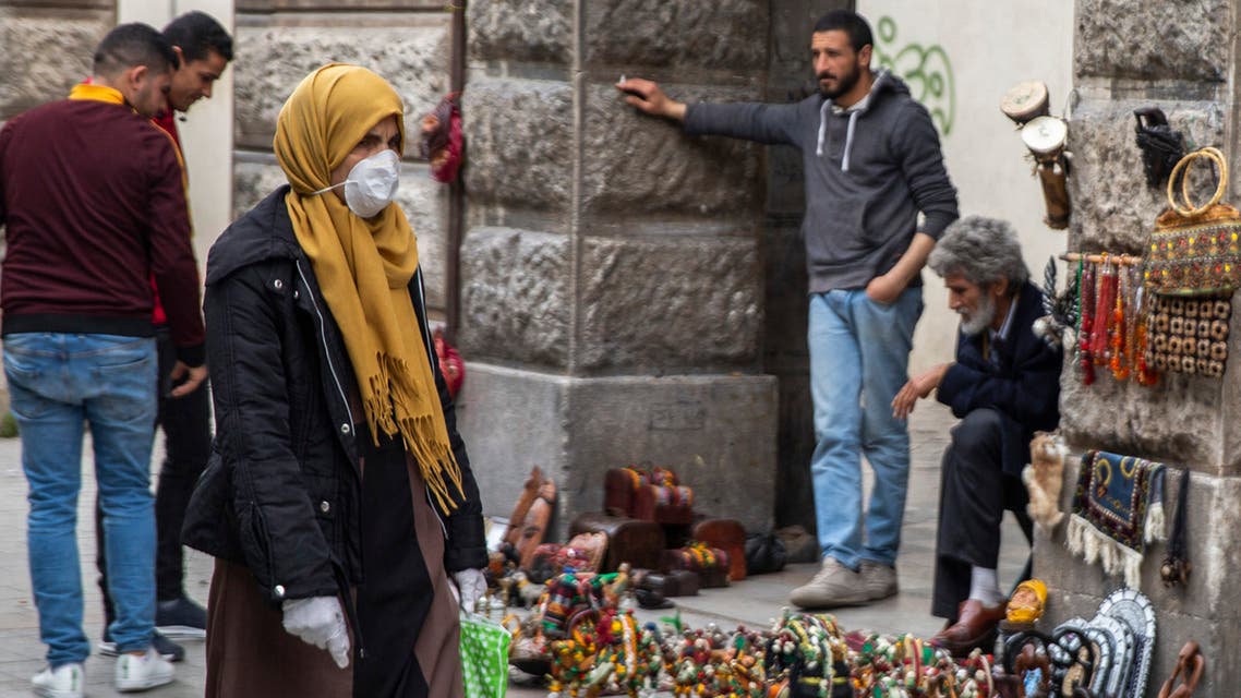 A woman wearing a mask walks past street vendors Tuesday, March 17, 2020 in Tunis. (AP)