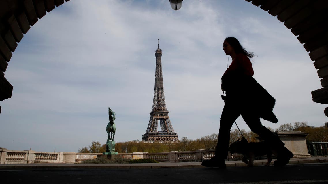 A woman walks her dog on a Paris bridge, with the Eiffel tower seen in background, during a nationwide confinement to counter the COVID-19, Tuesday, April 7, 2020. (AP)