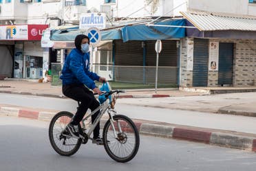 A man wearing a mask rides his bicycle after shopping in a deserted street of La Marsa, outside Tunis on March 26, 2020. (AP)