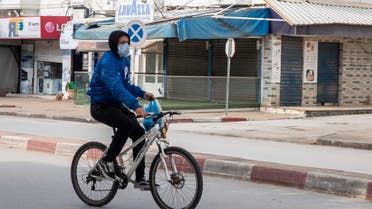 A man wearing a mask rides his bicycle after shopping in a deserted street of La Marsa, outside Tunis on March 26, 2020. (AP)