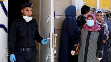 Palestinian policeman stands guard as a woman wearing a mask waits with other people outside a bank to withdraw cash, in Gaza City. (Reuters)