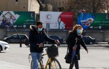 Syrians wearing face masks walk in front of posters informing about the novel coronavirus, in the capital Damascus on April 1, 2020. (AP)