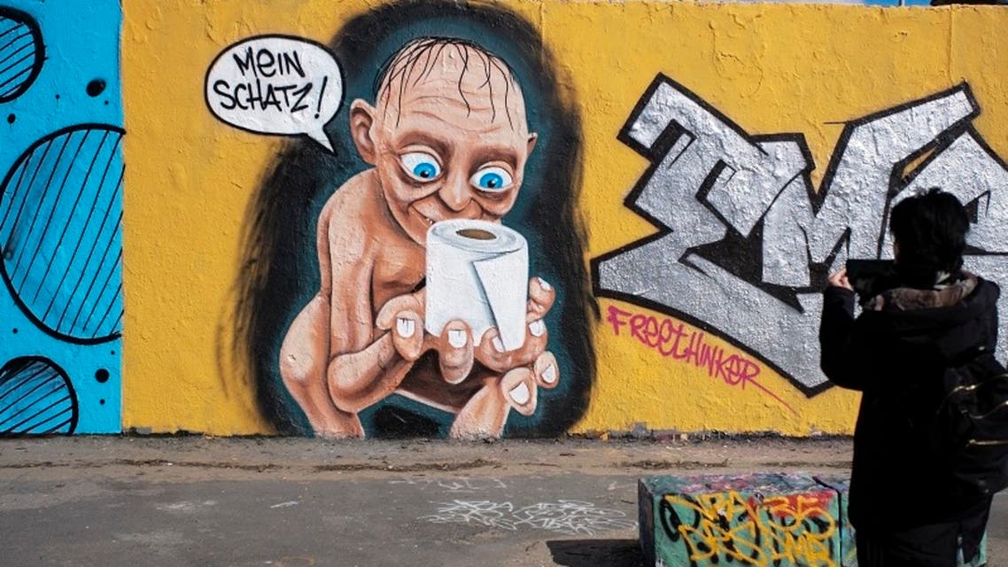 A woman takes a photo of a graffiti depicting the character of Gollum from Lord of the Rings, holding a roll of toilet paper and saying My precious, in the Mauerpark public park at the district Prenzlauer Berg in Berlin. (File photo: AP)