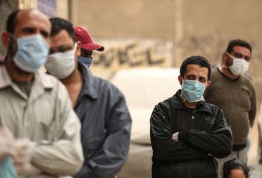 Egyptian men wearing masks wait outside a center of non-governmental organization Egyptian Food Bank to receive cartons with foodstuffs on April 05, 2020 in Cairo. (AFP) 