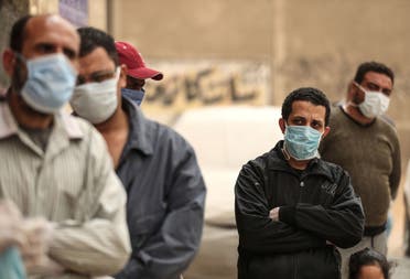 Egyptian men wearing masks wait outside a center of non-governmental organization Egyptian Food Bank to receive cartons with foodstuffs on April 05, 2020 in Cairo. (AFP)