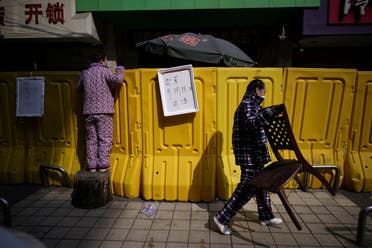 A resident pays for groceries by standing on a tree stump to peer over barriers set up to ring fence a wet market on a street in Wuhan, the epicentre of China's coronavirus disease outbreak, on April 1, 2020. (Reuters)